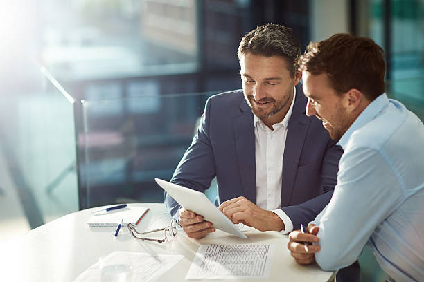Two professionals discussing work at a table with documents and a laptop